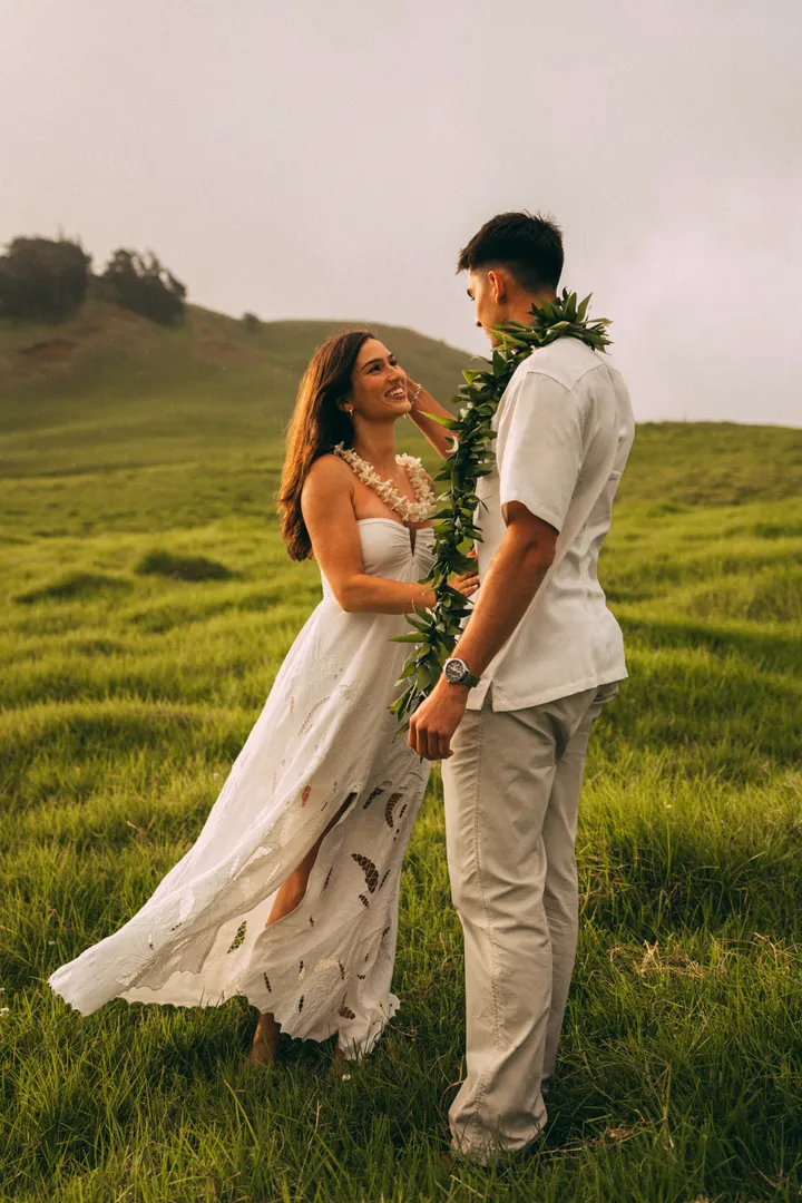 Kahalley and Rico standing together in a green Hawaiian pasture, Rico wearing a maile lei.