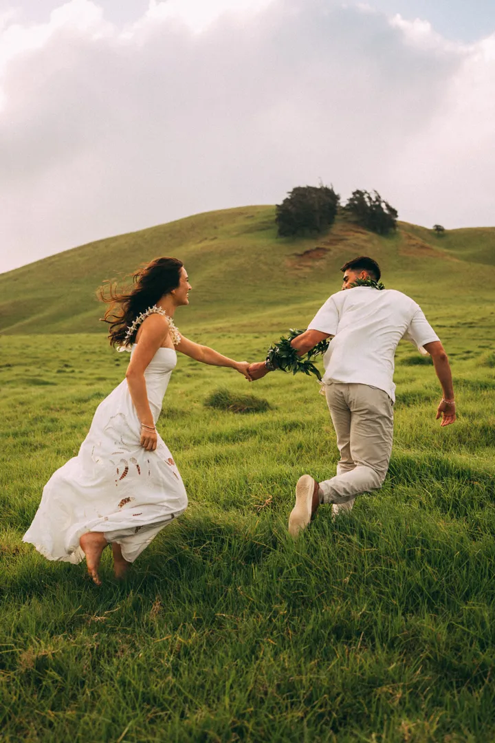 Kahalley and Rico running hand in hand through tall grass on a hillside.
